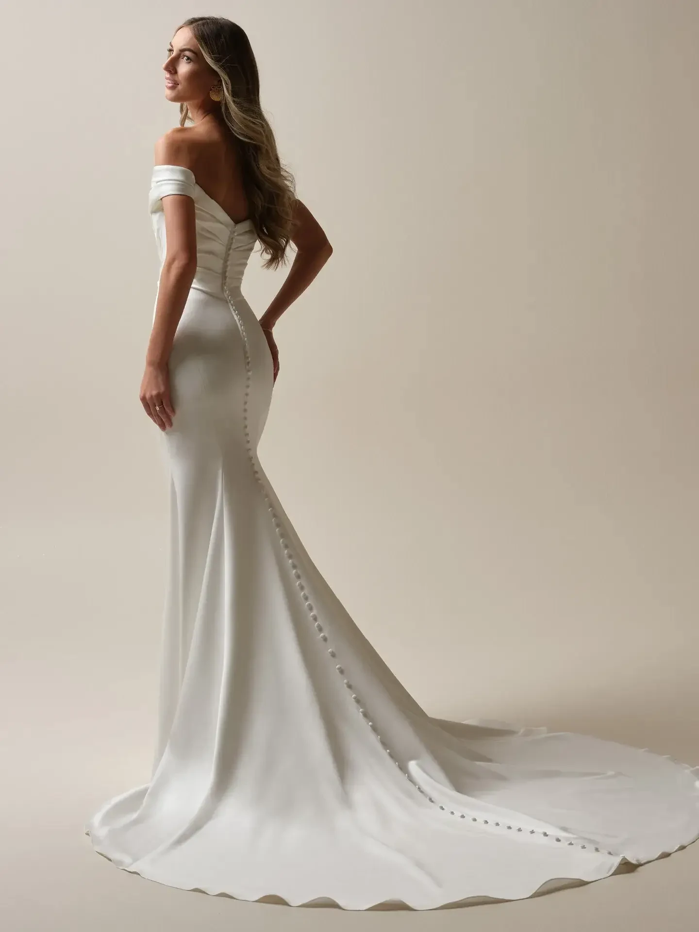 Model is wearing an off the shoulder satin ruched fitted wedding gown