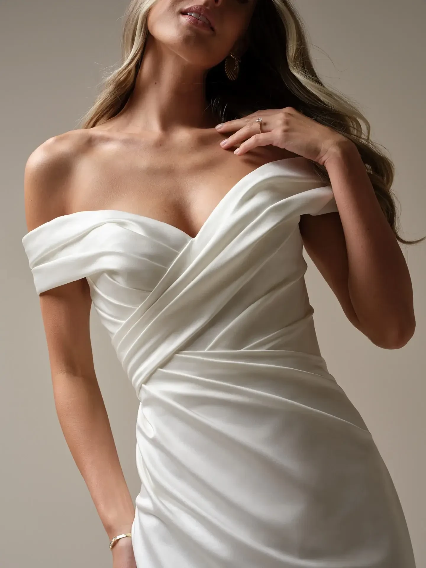 Model is wearing an off the shoulder satin ruched fitted wedding gown