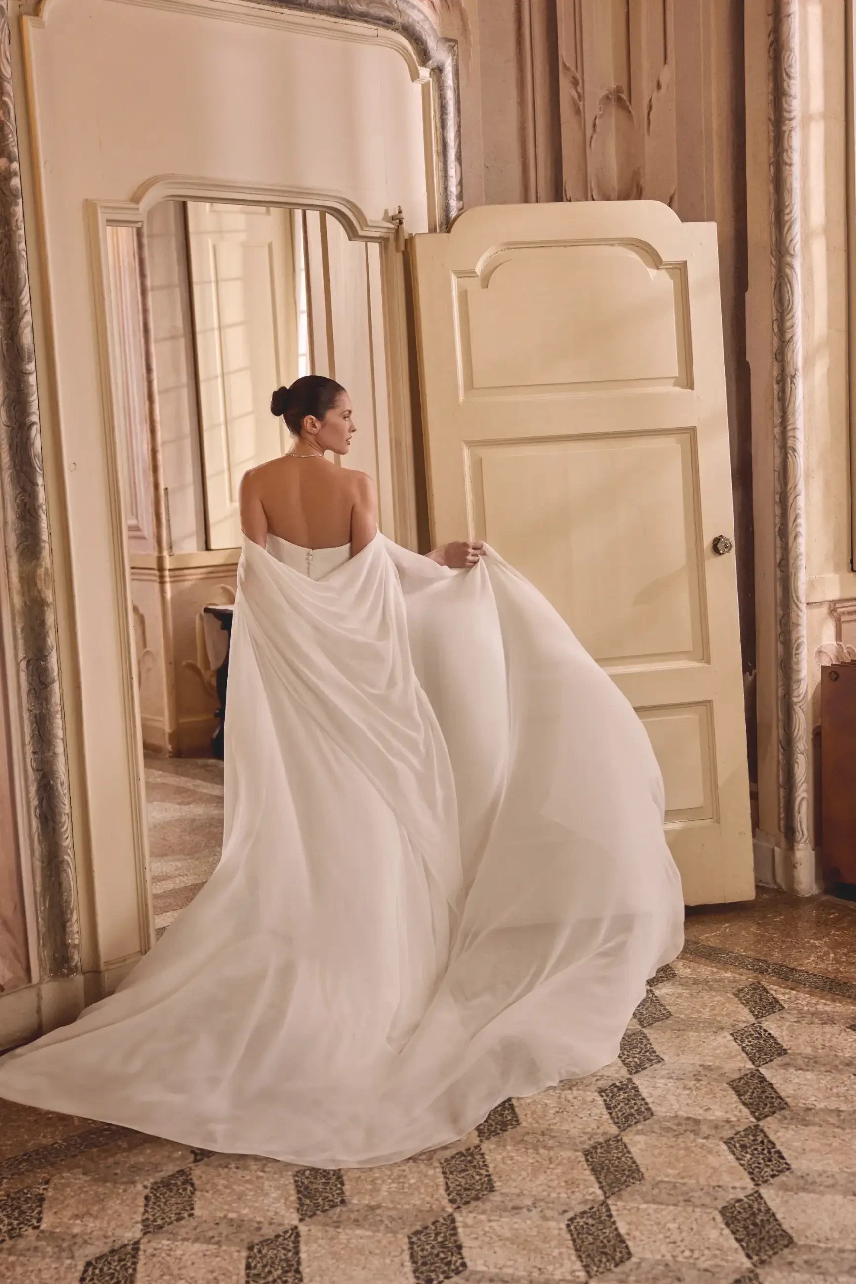 Model is wearing a strapless cat eye neckline fit and flare minimalist crepe wedding gown