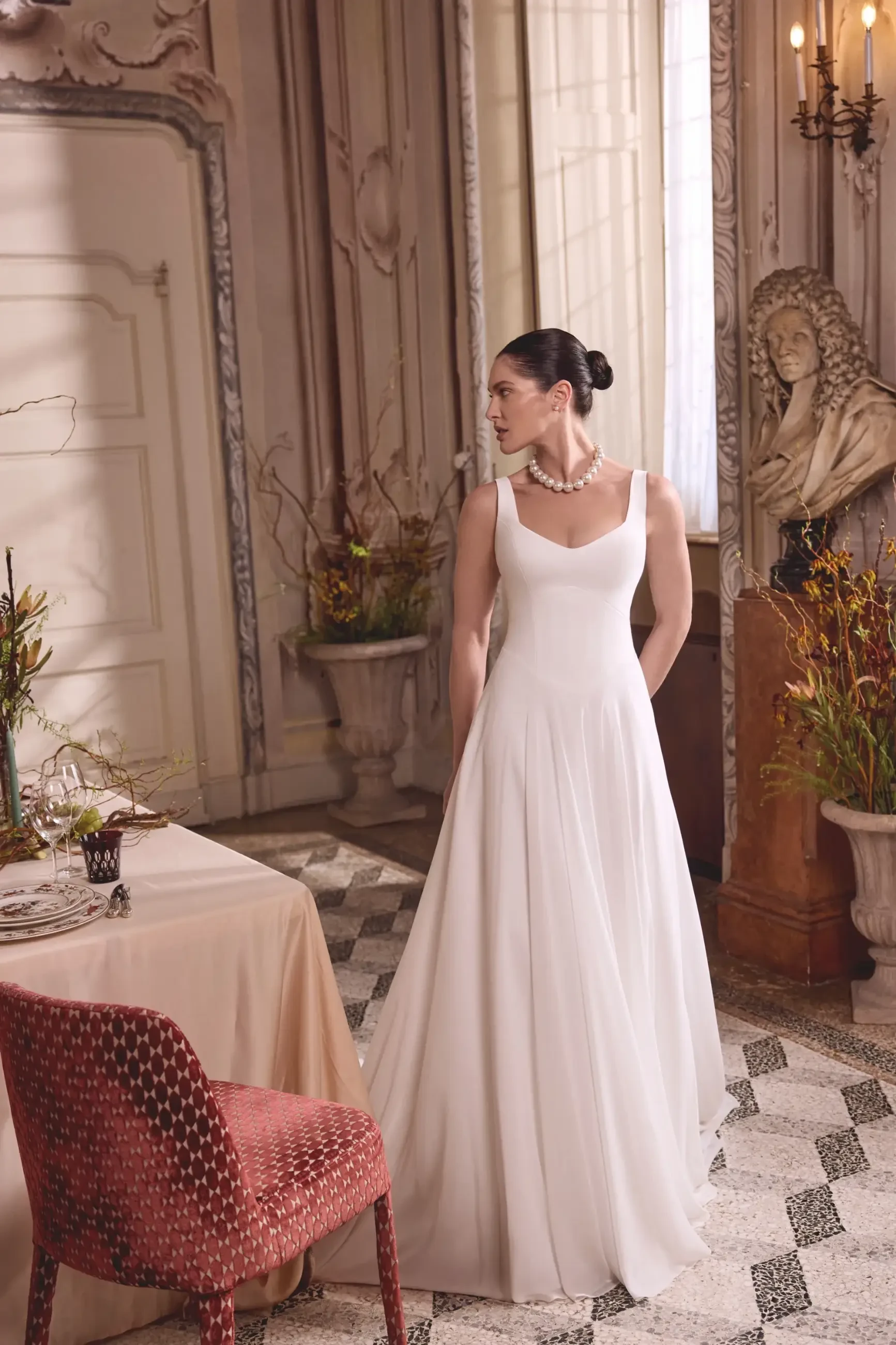 Model is wearing a sleeveless chiffon a-line wedding dress with a basque waist and sweetheart neckline