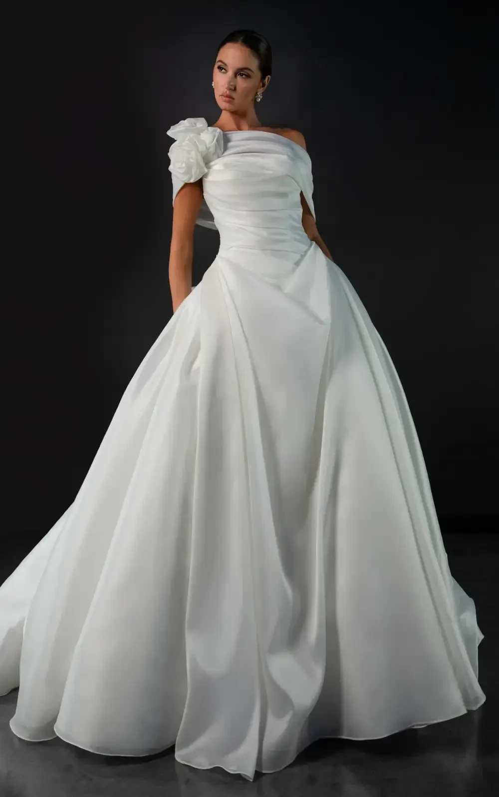 model is wearing an off the shoulder bridal gown with a 3d floral detail on one side